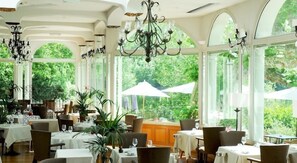 A restaurant with tables set for dining, large windows, and a view of greenery outside.