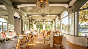 Un comedor con mesas dispuestas para una comida, sillas de mimbre y vistas a un lago.
