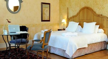 Habitación de hotel con una cama, un escritorio con una computadora portátil, dos sillas y una mesita de noche con una lámpara.