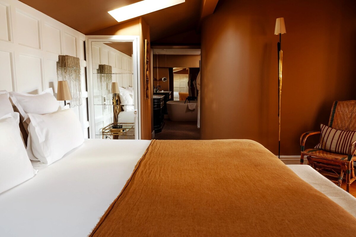 A hotel room with a large bed, a sitting area with a chair, and a bathroom visible through an open door.