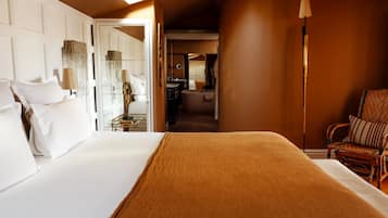 A hotel room with a large bed, a sitting area with a chair, and a bathroom visible through an open door.