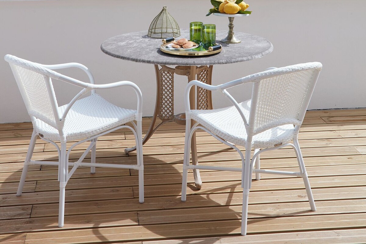 Una mesa redonda con dos sillas blancas sobre una terraza de madera con vista a un lago.