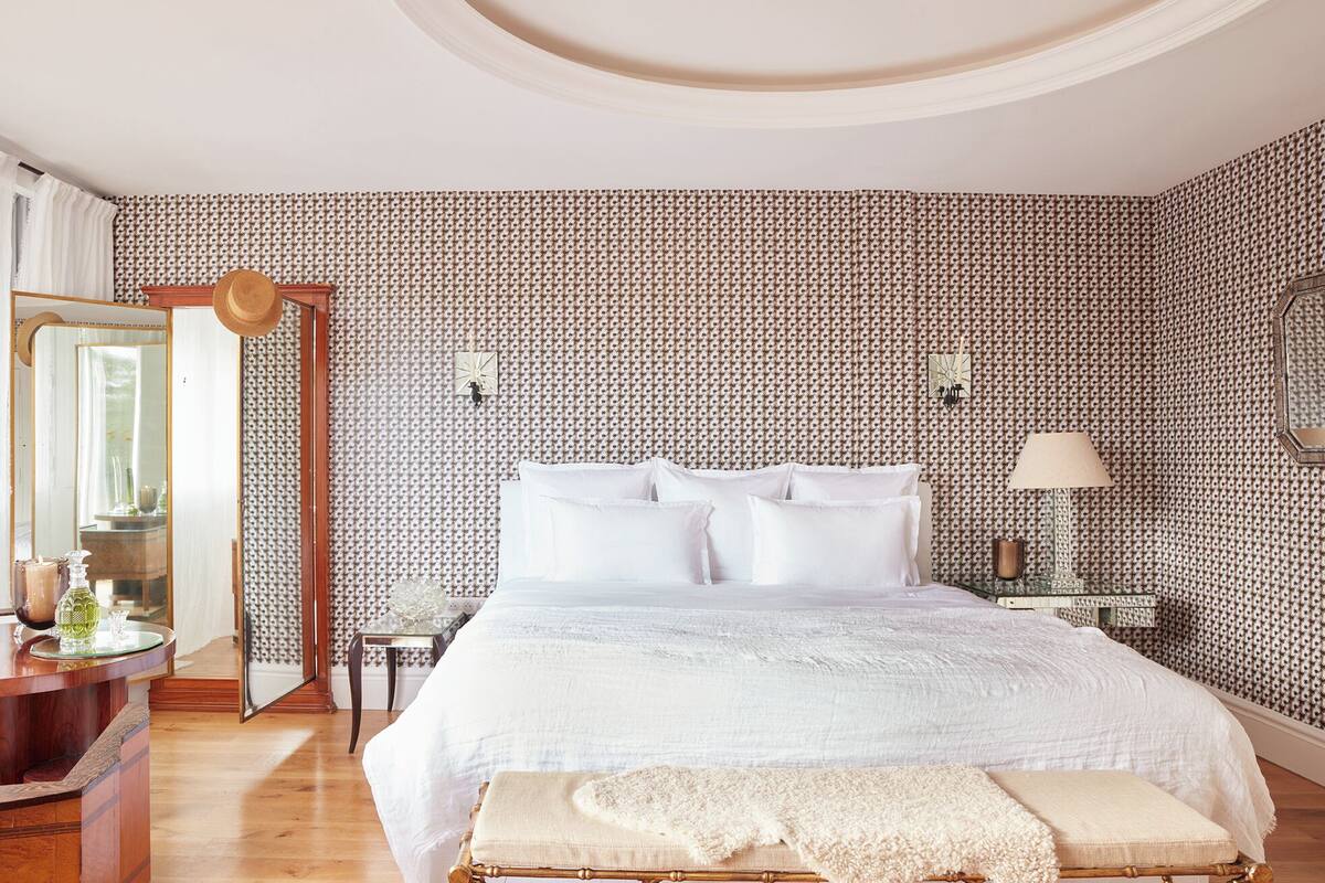 A bedroom with a large bed, a bedside table, a mirror, and a patterned wall.