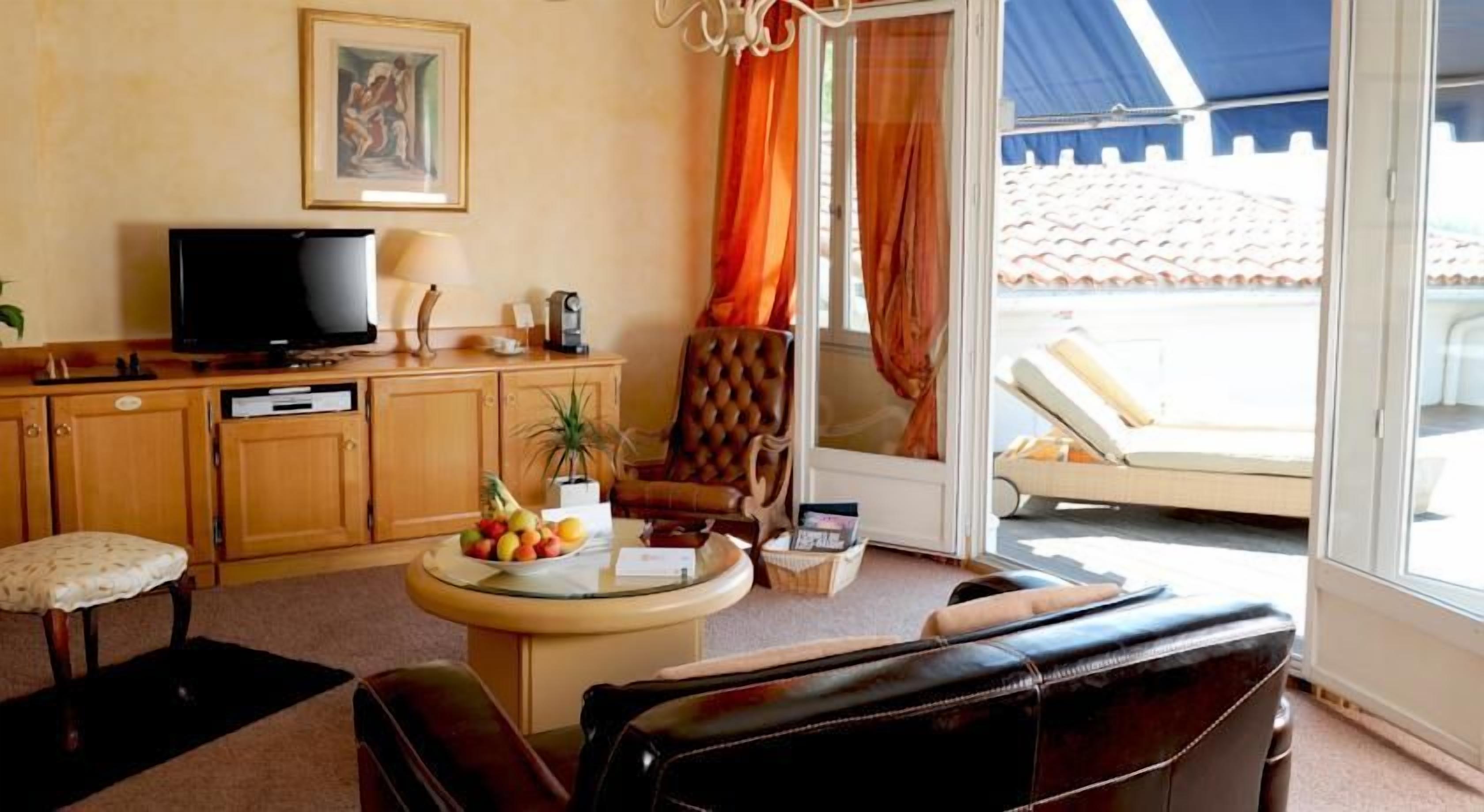 A living room with a television, a round table with fruits, a sofa, and a view of a pool through a glass door.