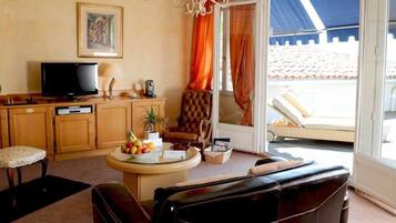 A living room with a television, a round table with fruits, a sofa, and a view of a pool through a glass door.