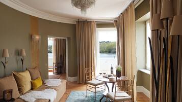 A room with a sofa, chairs, a table with a vase, and a view of a body of water.
