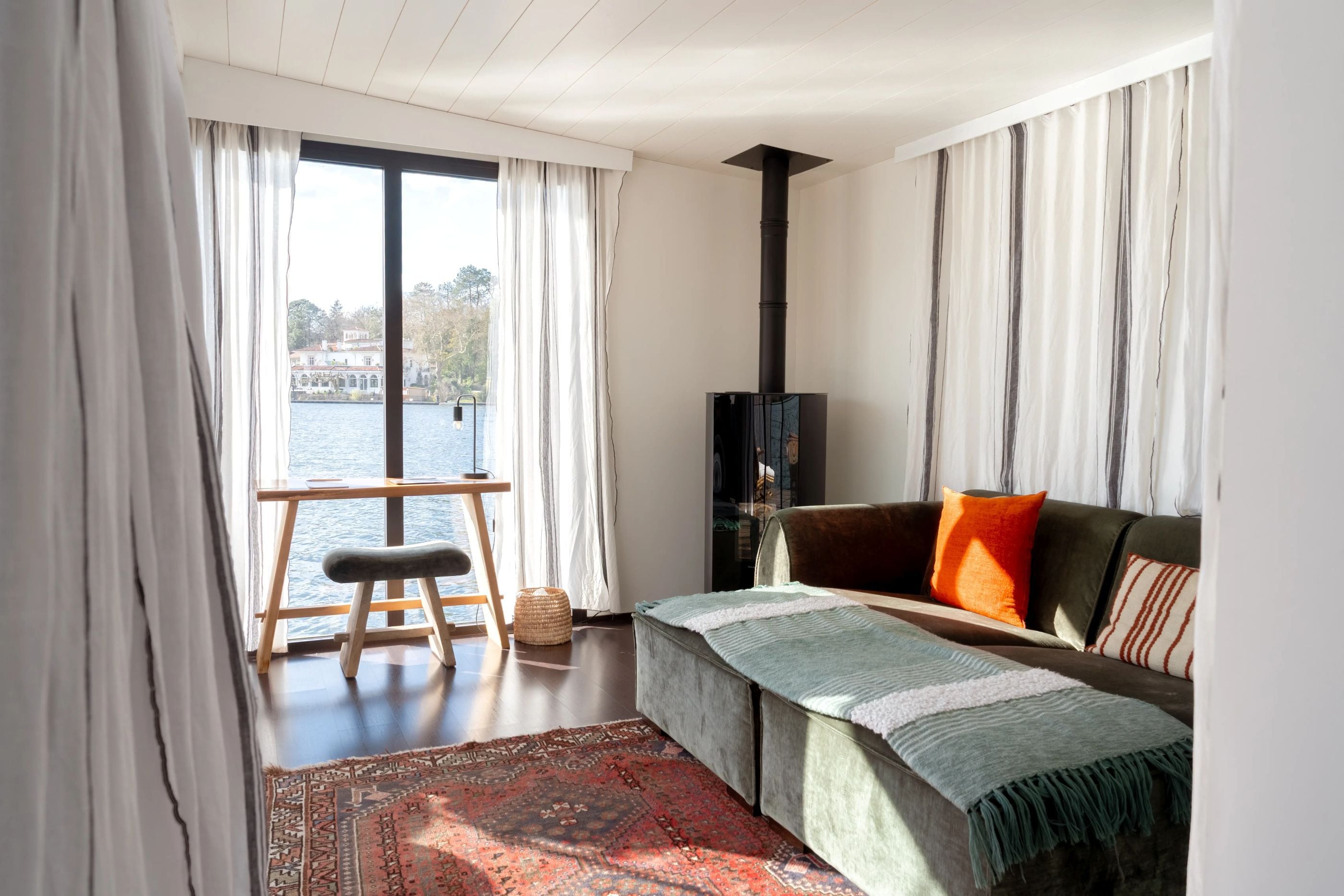 A living room with a view of a body of water, a sofa, a bench, and a rug.