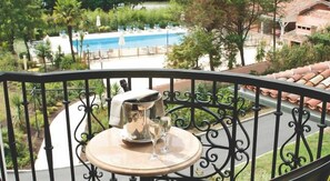 Un balcó amb taula, gerro i gots, davant d'una piscina i vegetació.