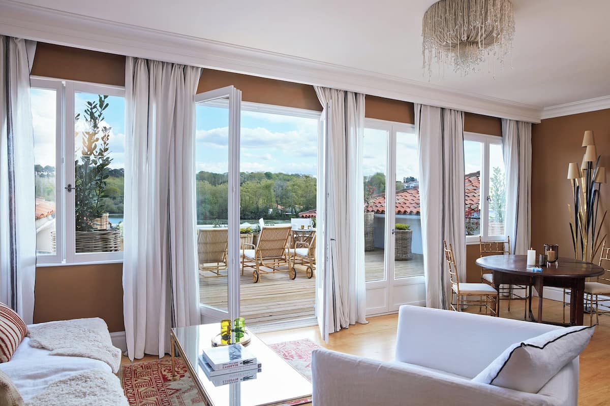 A spacious living room with a large window, a dining area with a table and chairs, and a view of the outdoors.