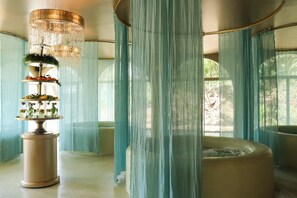 Quarto com uma banheira grande, cortinas leves e uma fonte decorativa.