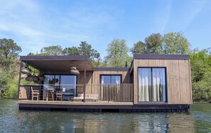 A floating house with a deck, a dining area, and a large window.