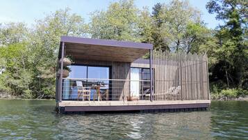 A floating house with a deck, windows, and a railing.