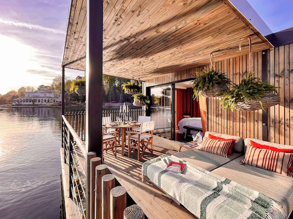 Una terraza de madera con sofá, sillas, una mesa de comedor y plantas colgantes.