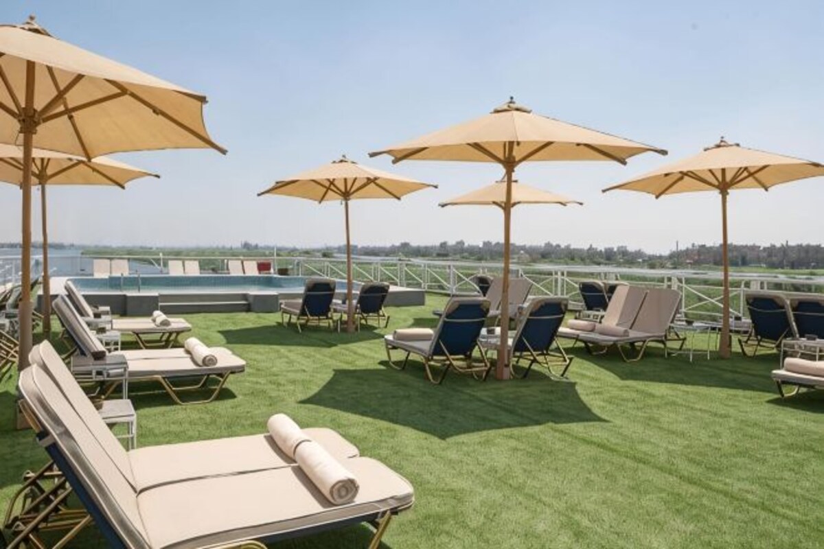 A rooftop lounge with sun loungers and umbrellas, a pool in the background, and a clear view of the city skyline.