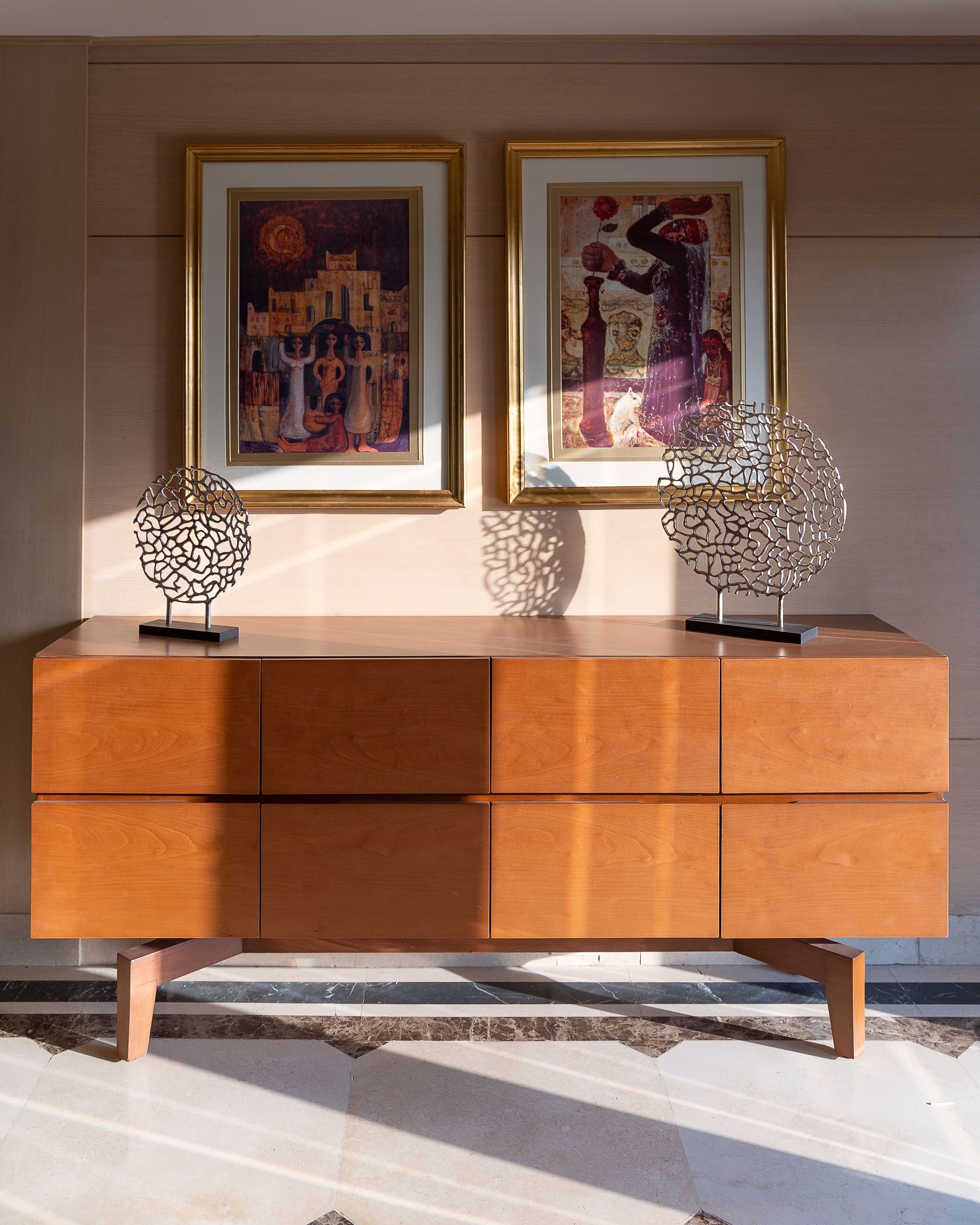 A wooden console table with two framed artworks and two abstract metal sculptures.