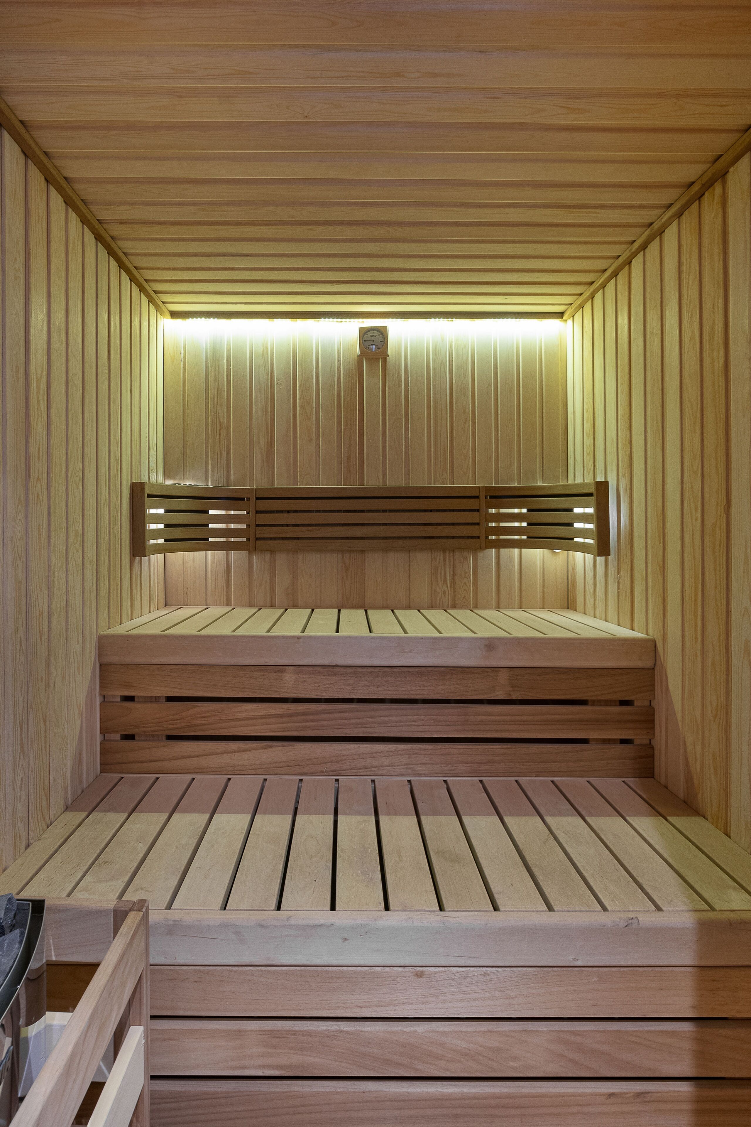 A sauna with wooden benches and slatted backrests, illuminated by overhead lights.