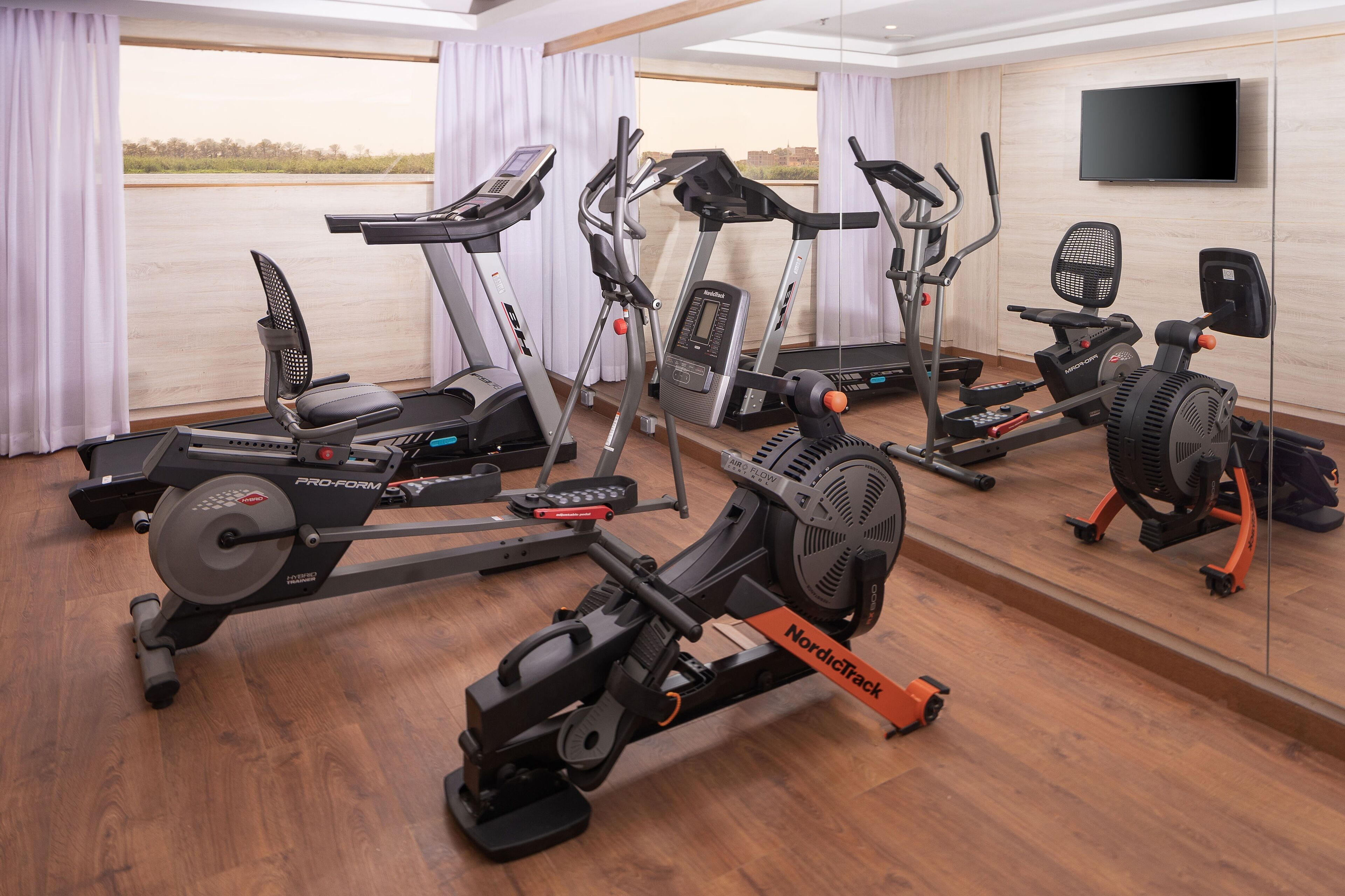 Un gimnasio con diversos equipos de ejercicio, incluyendo cintas de correr, una elíptica y una máquina de remo.