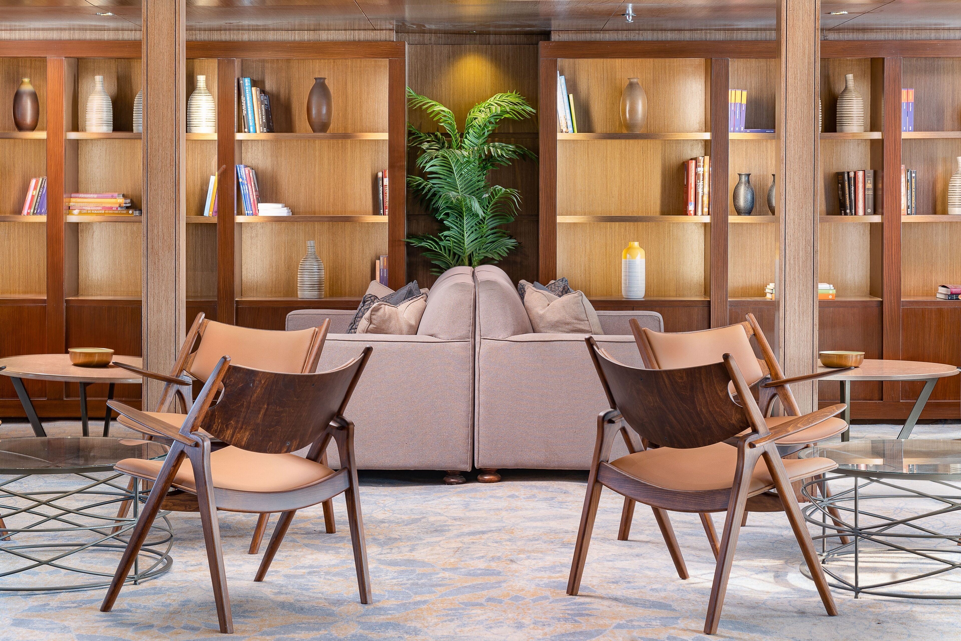 A lobby with a sofa and chairs, wooden bookshelves, and a potted plant.