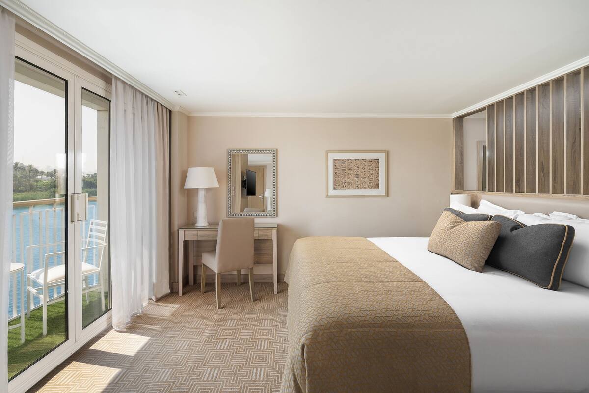 Une chambre d’hôtel avec un grand lit, un bureau avec une chaise, un miroir et une vue sur l’extérieur.