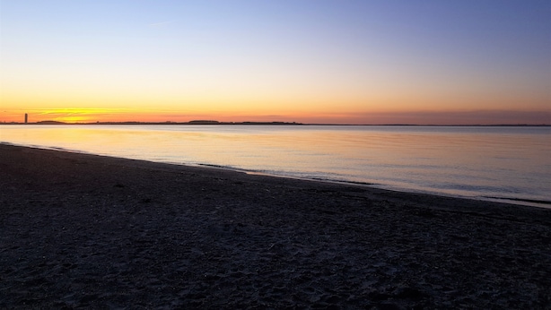 A beach with a clear sky and calm water during sunset.