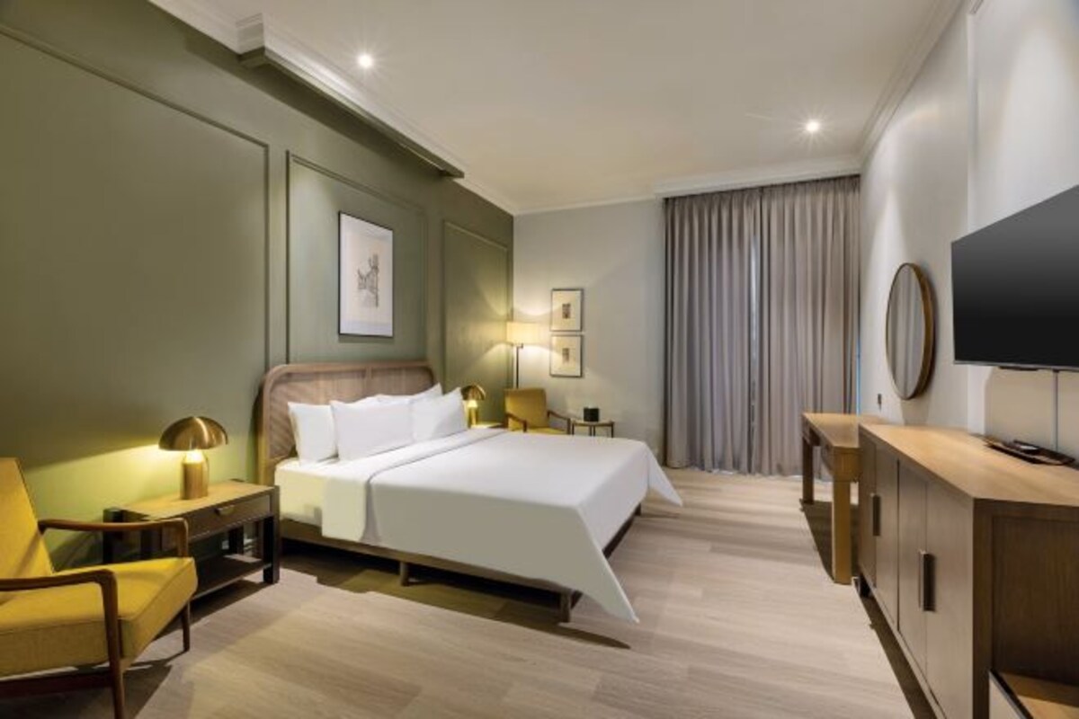 A hotel room with a bed, a TV, a desk, and a chair.