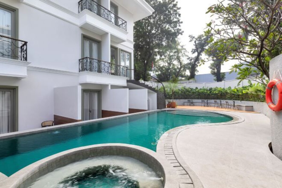 Een zwembad met een jacuzzi, omringd door een wit gebouw met balkons.