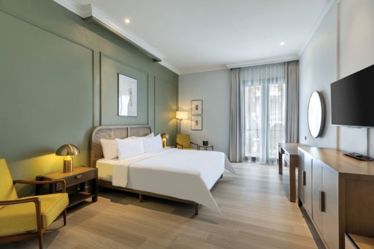 Een hotelkamer met een bed, bureau, stoel, televisie en raam met gordijnen.