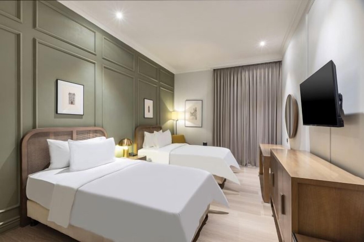 Una camera d'albergo con due letti, una cassettiera in legno, una TV a schermo piatto e quadri appesi alle pareti.
