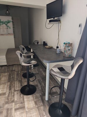 Un espace repas moderne comprenant une longue table, quatre tabourets de bar, un téléviseur à écran plat fixé au mur et un élément décoratif mural.