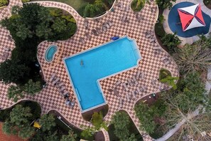 An aerial view of a swimming pool with checkered flooring, surrounded by lounge chairs and palm trees.