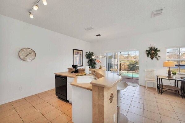 A kitchen with a dishwasher, a sink, and a countertop with a coffee maker. There is a clock on the wall and a plant on the counter.