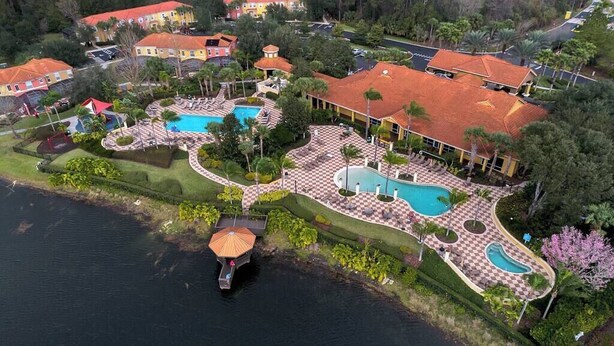 An aerial view of a resort with multiple swimming pools, a water feature, and a variety of buildings with red-tiled roofs. - Encantada - 4 bed 3 bath lakefront corner house (Kissimmee)
