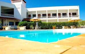 A hotel with a swimming pool, outdoor seating, and a white building with balconies. - Galu Inn (Diani Beach)