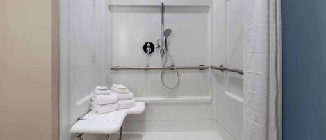A small, enclosed shower area with a white bench, a towel rack, and a showerhead.