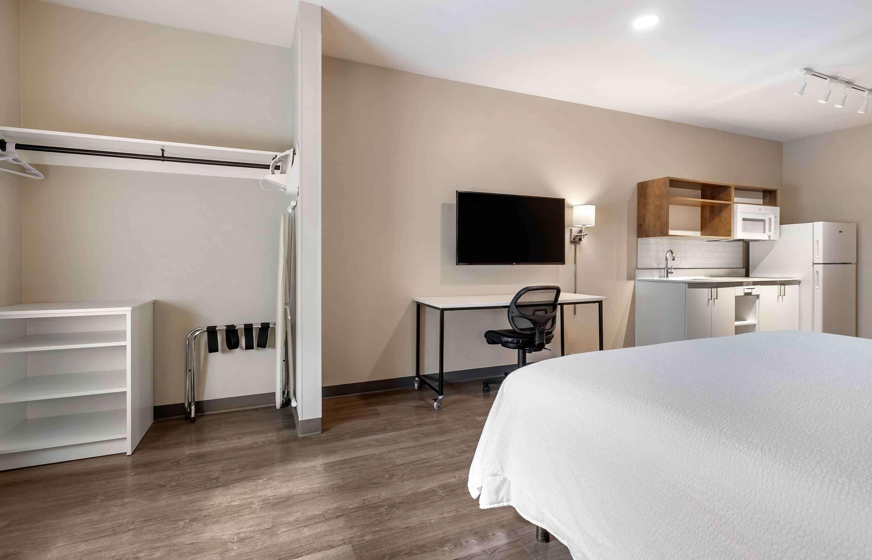 Habitació d'hotel amb llit, escriptori, cadira, televisió i petita cuina.