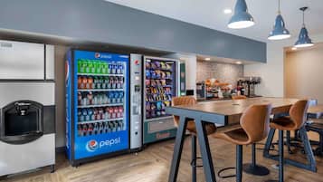 Un área de cocina moderna con una isla grande, taburetes de bar y máquinas expendedoras que incluyen marcas como Pepsi y RiverSide.