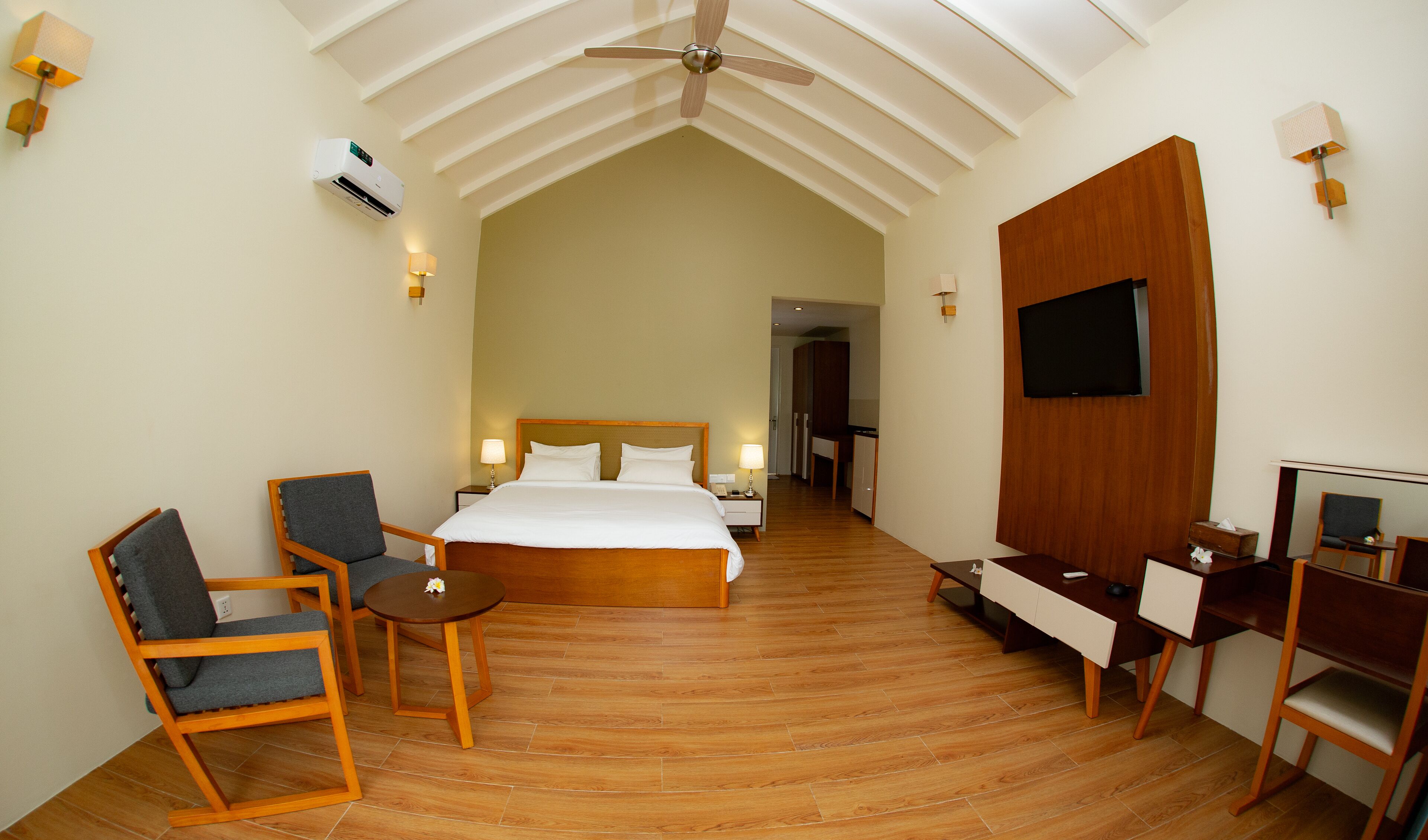 Habitación de hotel con cama, escritorio, silla, televisor y ventilador de techo.