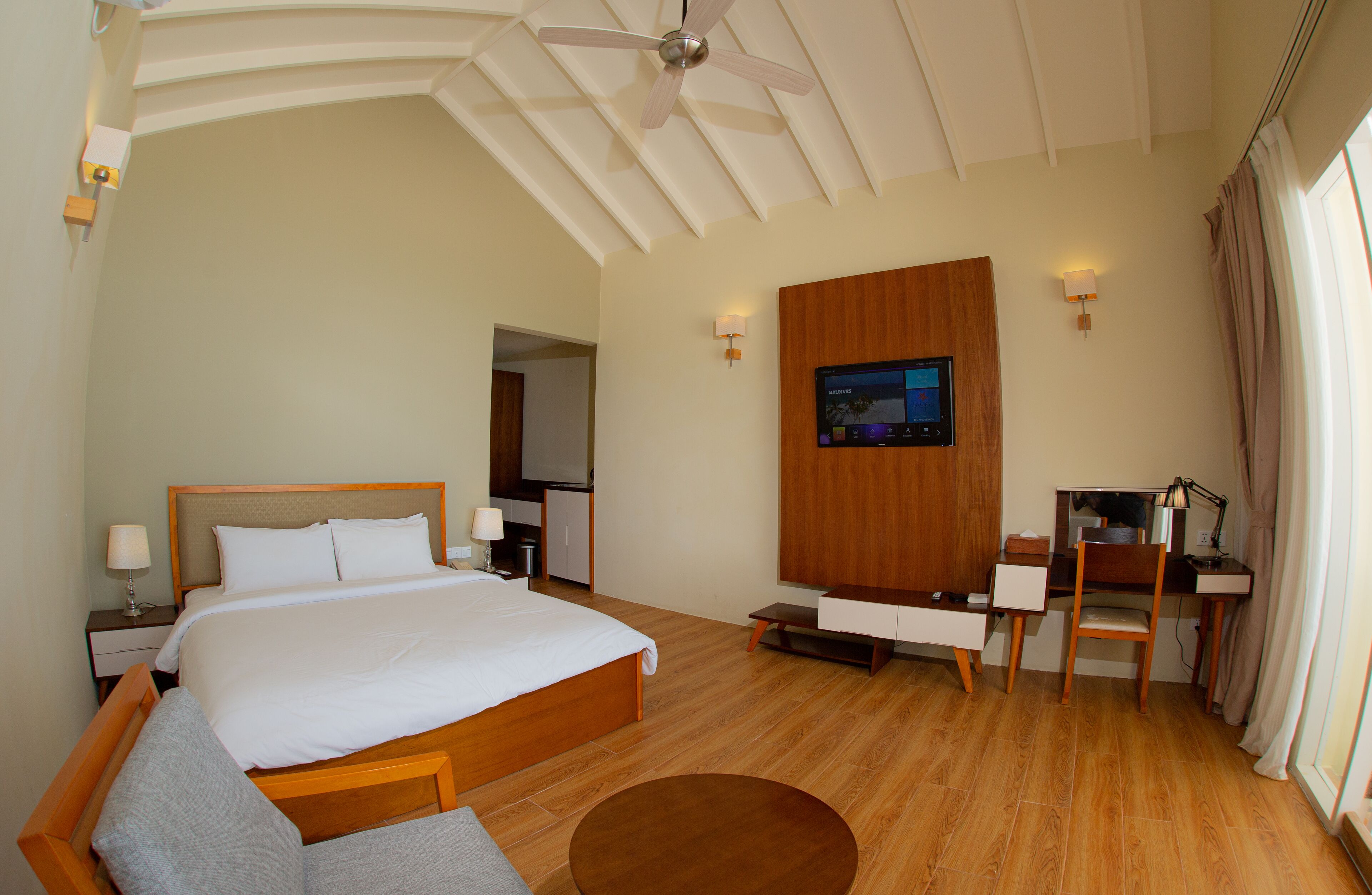 Ein Hotelzimmer mit einem großen Bett, einem Schreibtisch, einem Sessel, einem Fernseher und einem Deckenventilator.