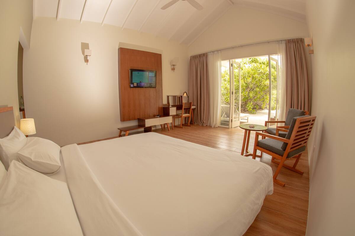 A hotel room with a large bed, a desk with a chair, a television, and a balcony with curtains.