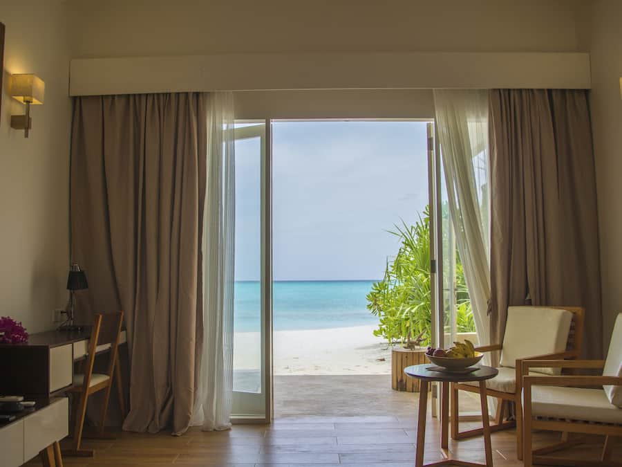Una habitación con escritorio, sillas, una mesita con frutero y vista a la playa a través de un ventanal.