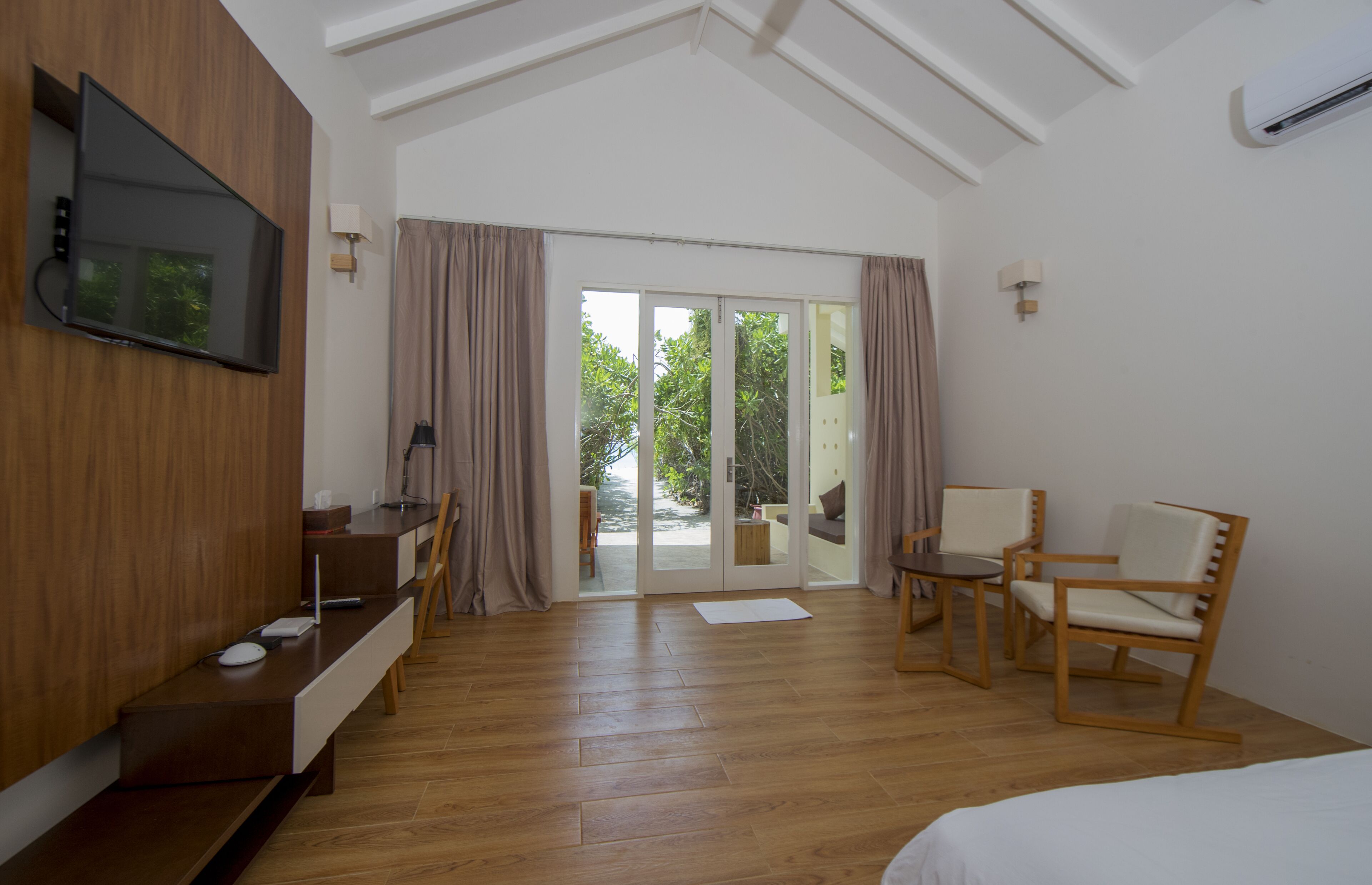 Une chambre d’hôtel avec un plancher en bois, un lit, un téléviseur fixé au mur, un bureau avec un ordinateur, une chaise et une vue sur l’extérieur grâce à une porte-fenêtre coulissante.