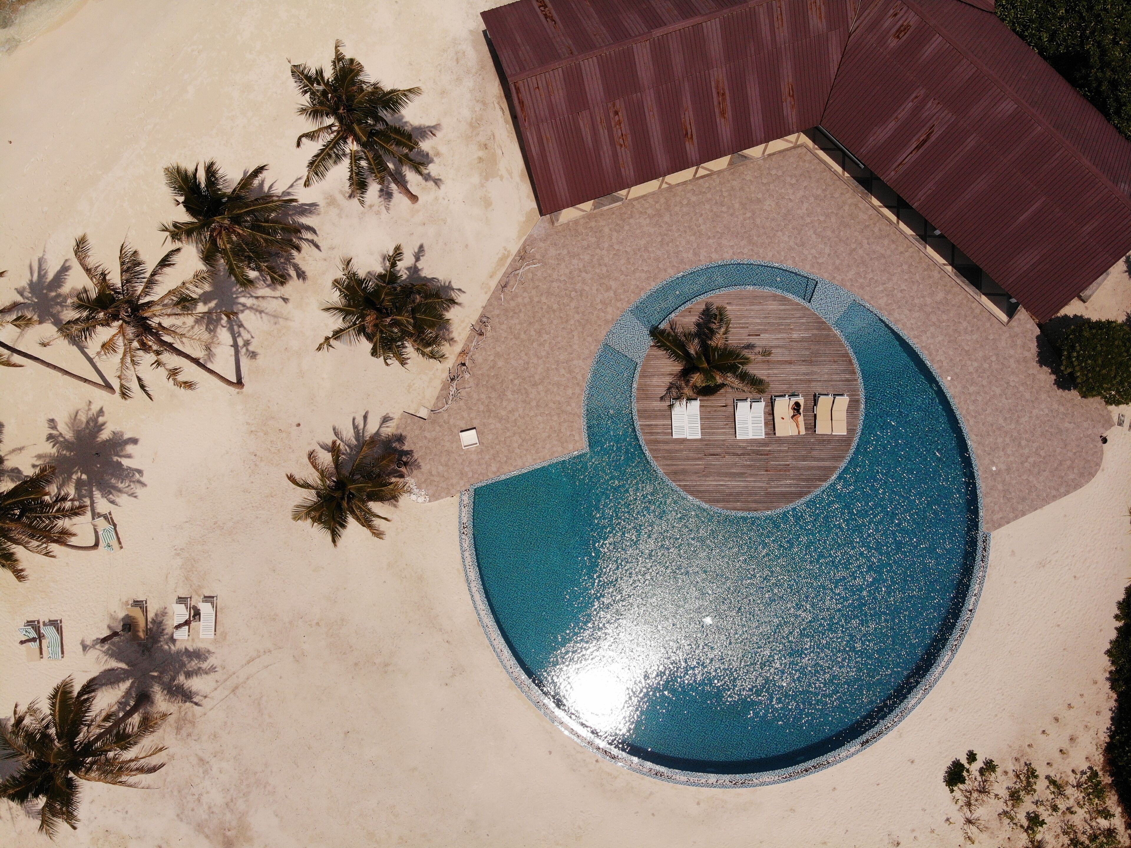 An aerial view of a resort with a circular swimming pool surrounded by lounge chairs and a wooden deck.