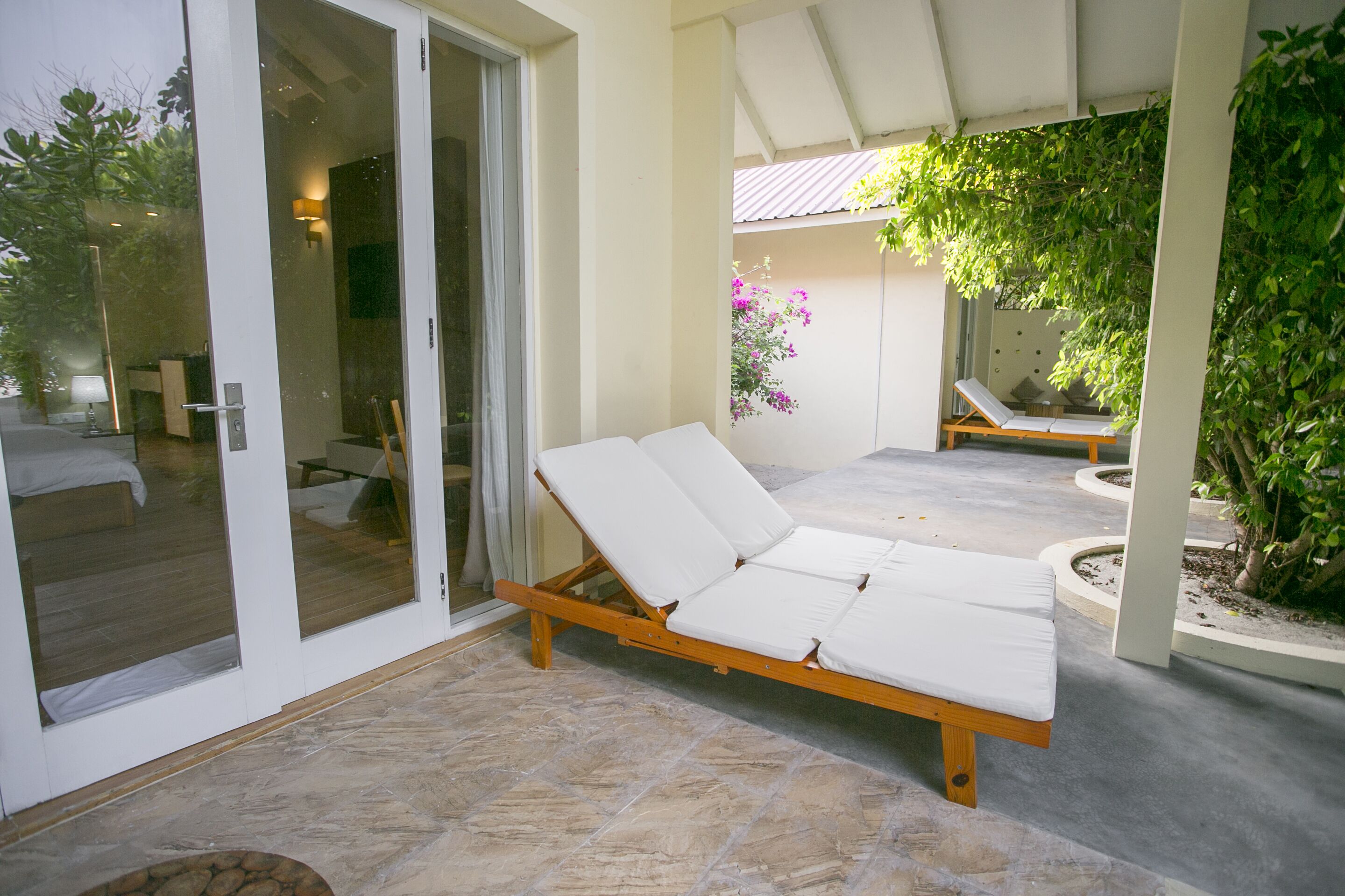 A sunlit outdoor lounge area with a wooden lounge chair and a glass door leading to a room.