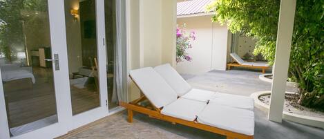 A sunlit outdoor lounge area with a wooden lounge chair and a glass door leading to a room.