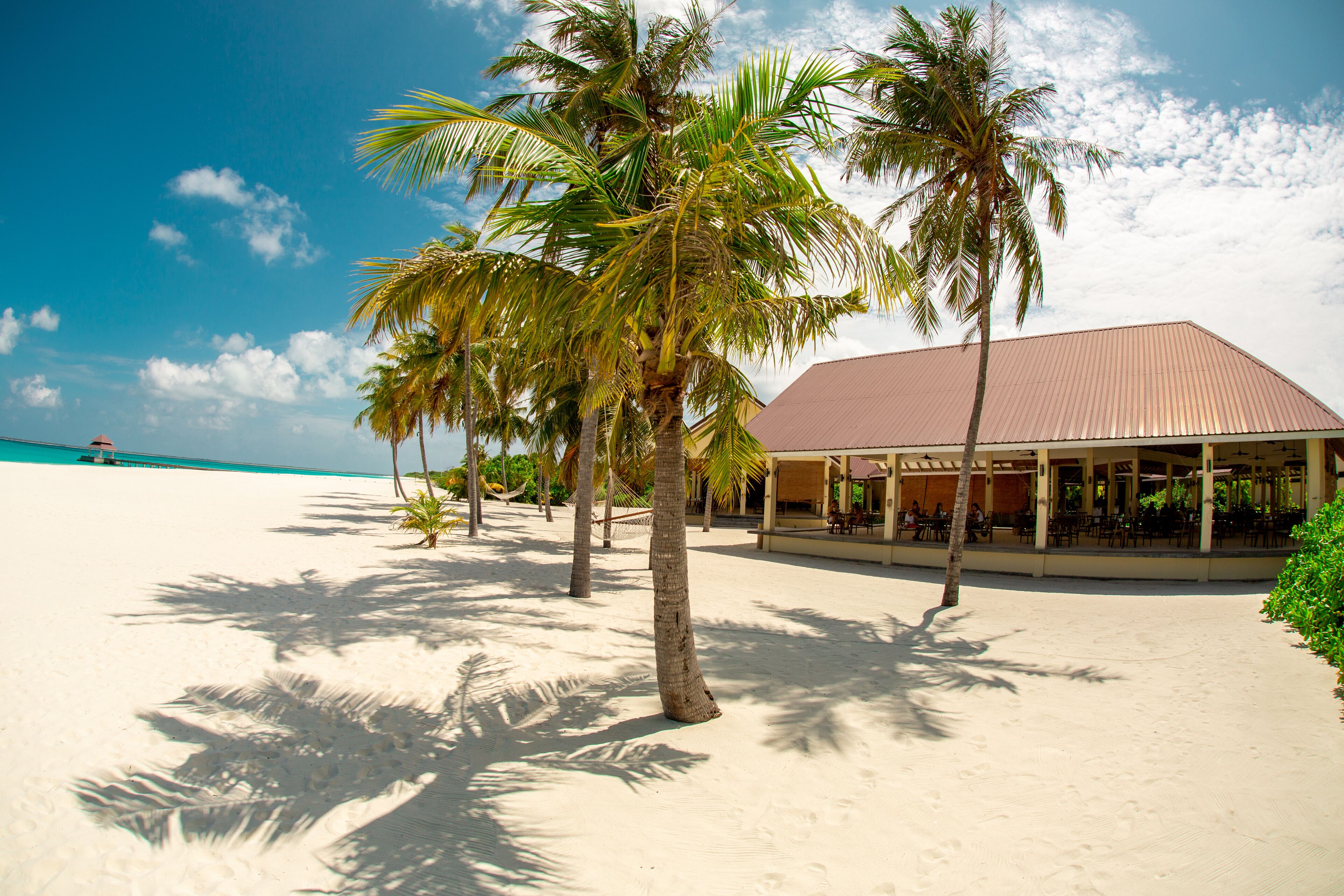 Ein Strandresort mit Palmen, einem Sandstrand und einem Gebäude mit rotem Dach.