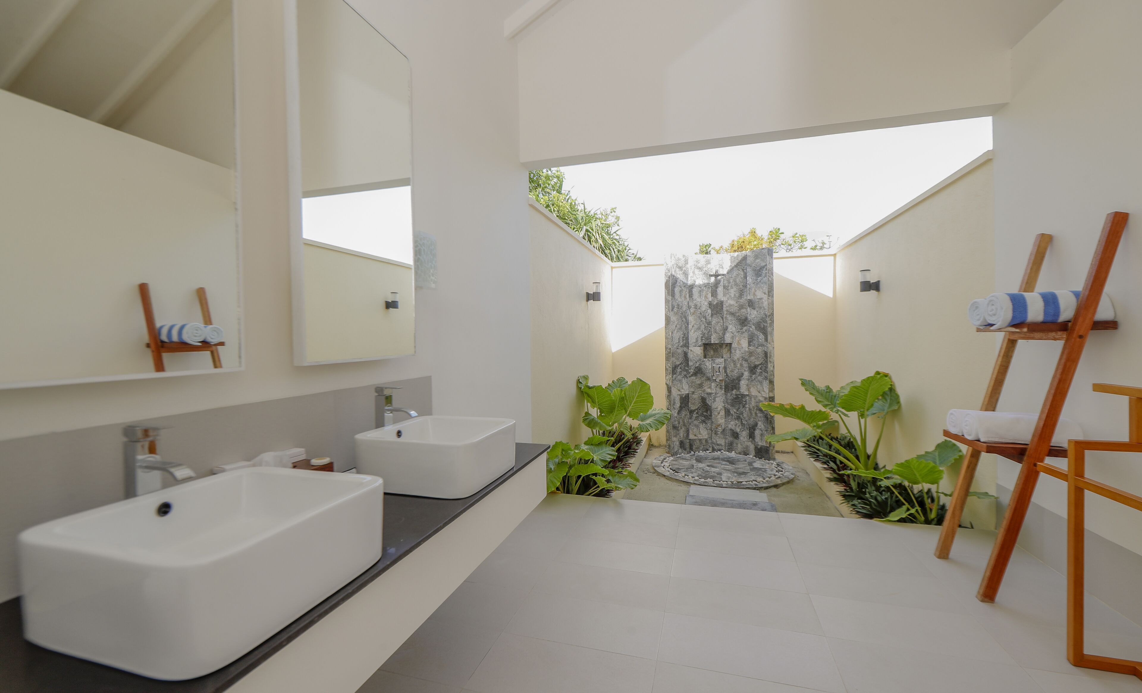 Ein modernes Badezimmer mit zwei Waschbecken, einem großen Spiegel und einer Duschkabine mit Steinwand.