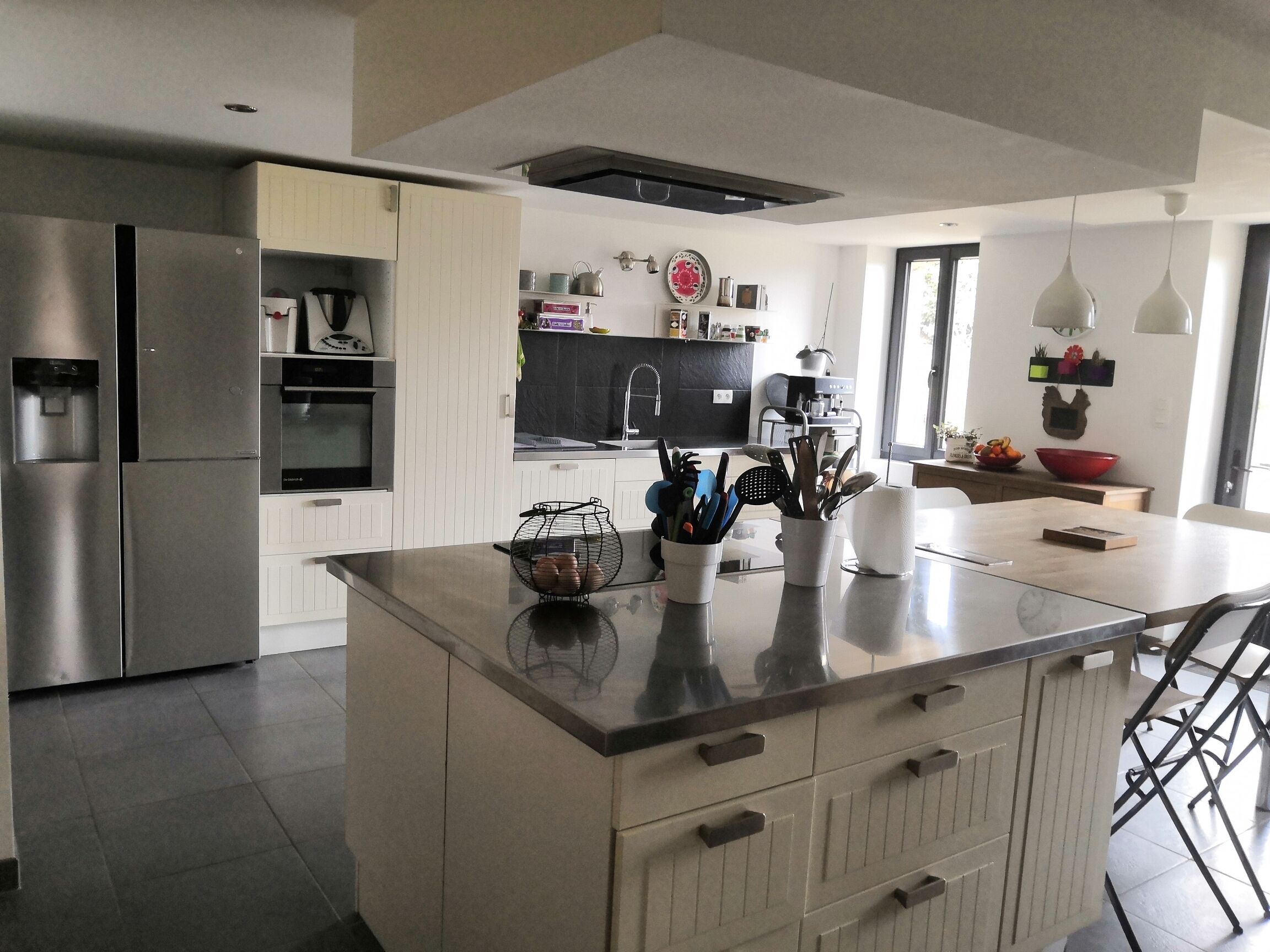 A modern kitchen with a central island, stainless steel appliances, and a variety of utensils and cookware.