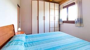 Un dormitorio con cama, mesita de noche, armario y ventana con cortinas.
