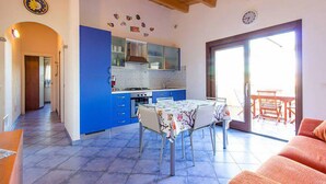 Una cocina con armarios azules, una mesa de comedor con sillas y un amplio ventanal corredera que da a un espacio exterior.