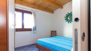 Un dormitorio con cama, ventana con cortinas, un radiador y una puerta con picaporte.